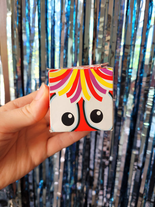 Colourful small square box decorated with cartoon close up of the red nose's eyes and hair