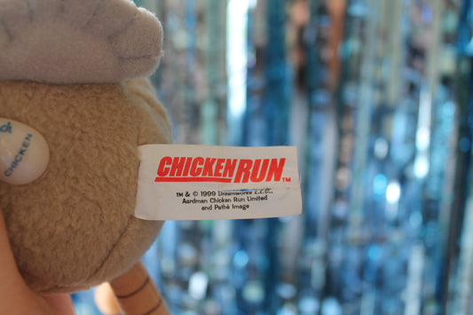 Detail of the label with a tear down the middle. Label reads CHICKEN RUN. Tm 1999 Aardman Chicken Run Limited and Pathé Image. Image shows part of a small egg shaped tag on the back of the toy that reads 'Top Notch Chicken'