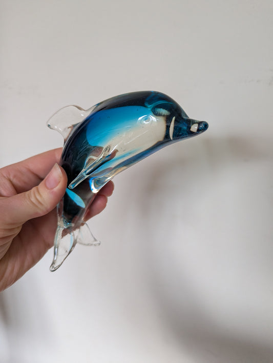 Hand holding a blue and clear dolphin glass ornament against a white background
