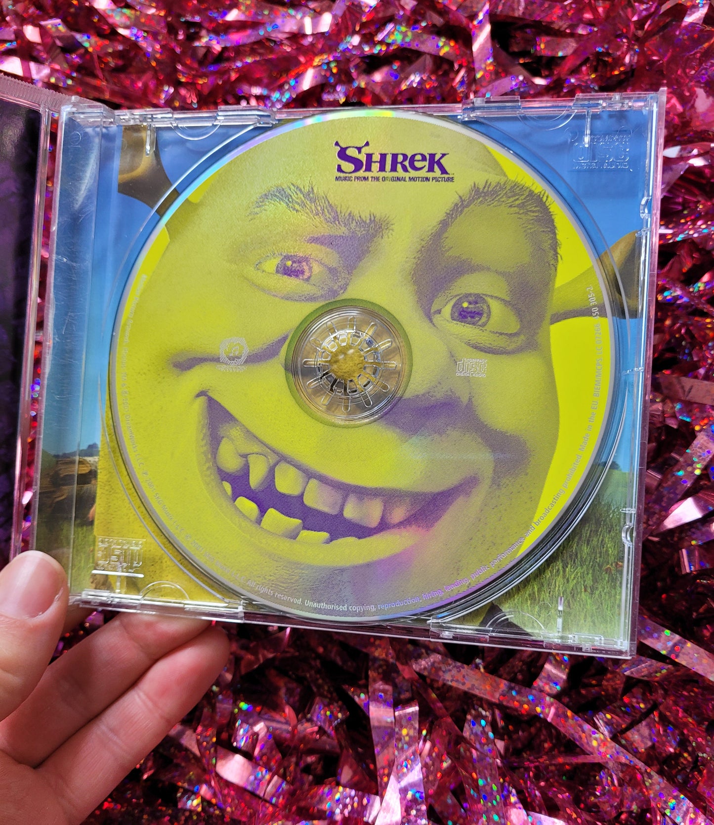 The inside of the opened CD case. The CD itself is bright green and has a close up of Shrek's grinning face on it 