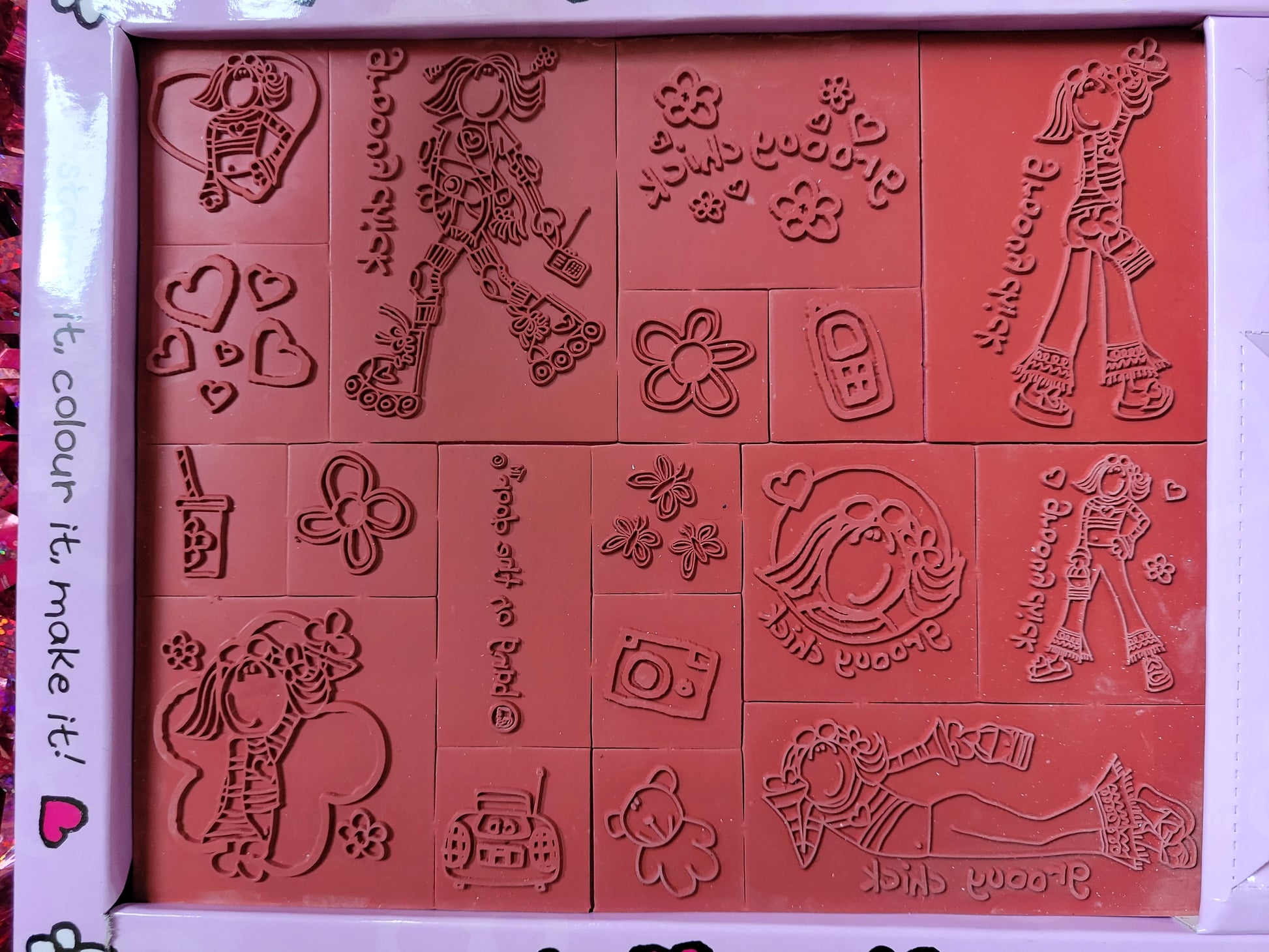 Close up of the red rubber stamps including: 00s style camera, phone and cd player/radio, flowers, butterflies, a teddy, love hearts, a drink with a straw in it, groovy chick in different poses such as waving, lying down, using roller skates and posing with her hand on her hip 