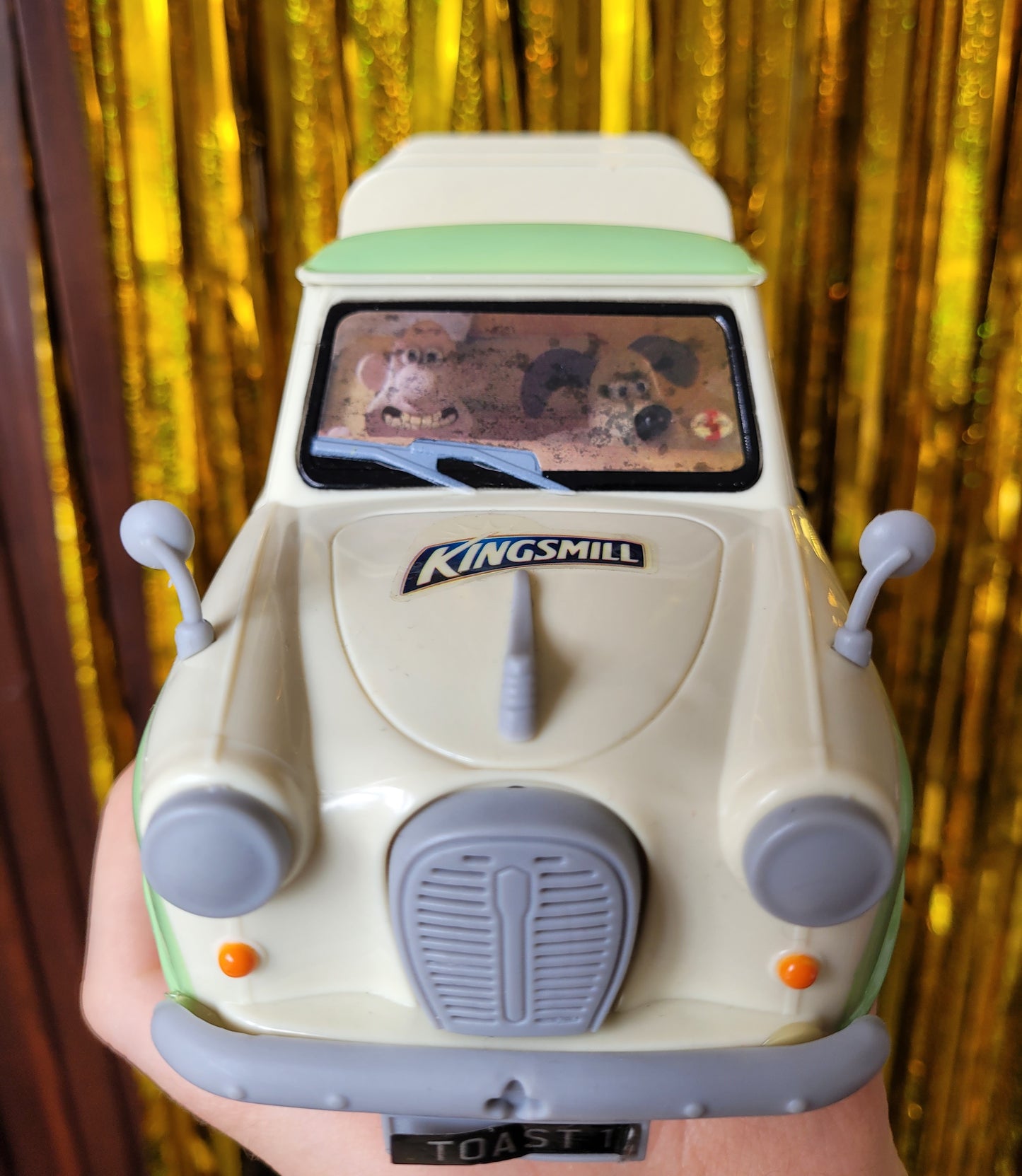 Mint green and cream van figurine. The windscreen is a sticker of Wallace grinning and Gromit looking bemused and slightly alarmed. The van has a Kingsmill sticker on the bonnet and a license plate that reads 'TOAST 1' The front windscreen sticker is water damaged with darkened water marks. The faces are still visible. 