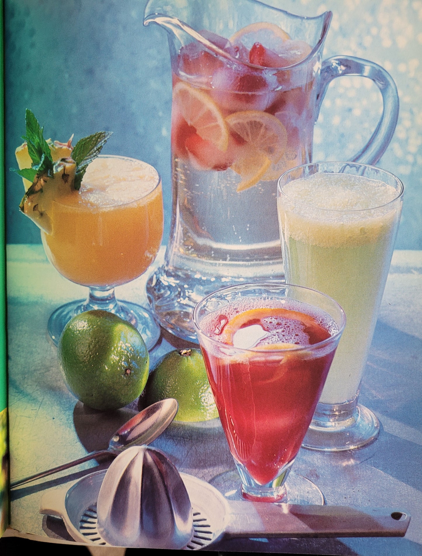 Assorted colourful cocktails and fresh fruit with cocktail making equipment on a table. The photograph has been edited with a 90's space-age sort of silver blue filter