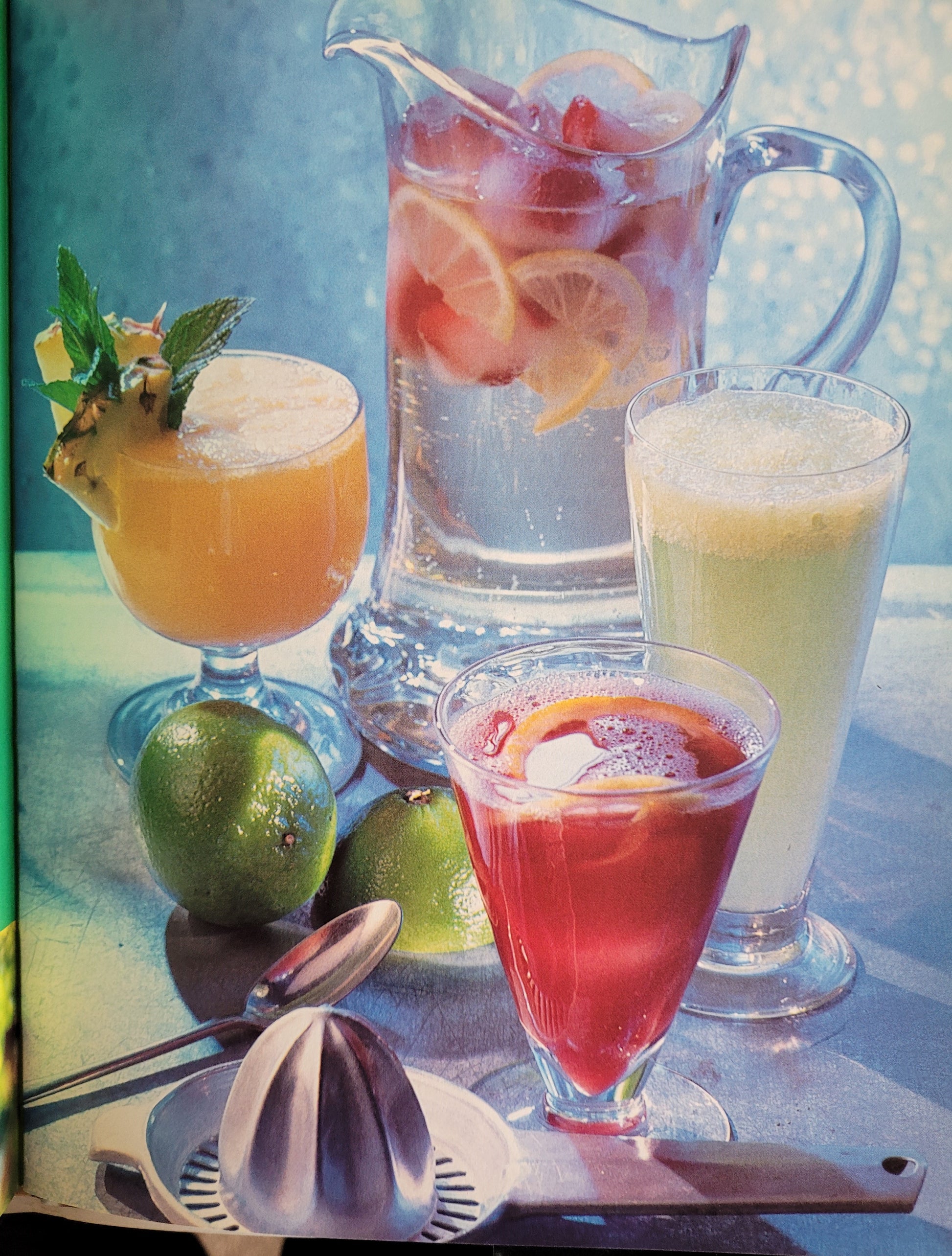 Assorted colourful cocktails and fresh fruit with cocktail making equipment on a table. The photograph has been edited with a 90's space-age sort of silver blue filter