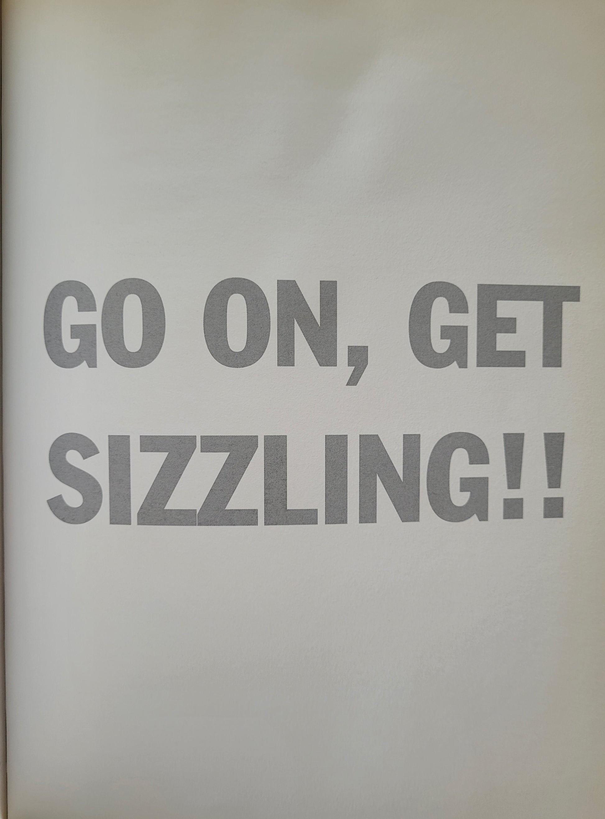 A page of the book that reads in bold, grey text all caps saying 'GO ON, GET SIZZLING!!' in the centre of a plain white page