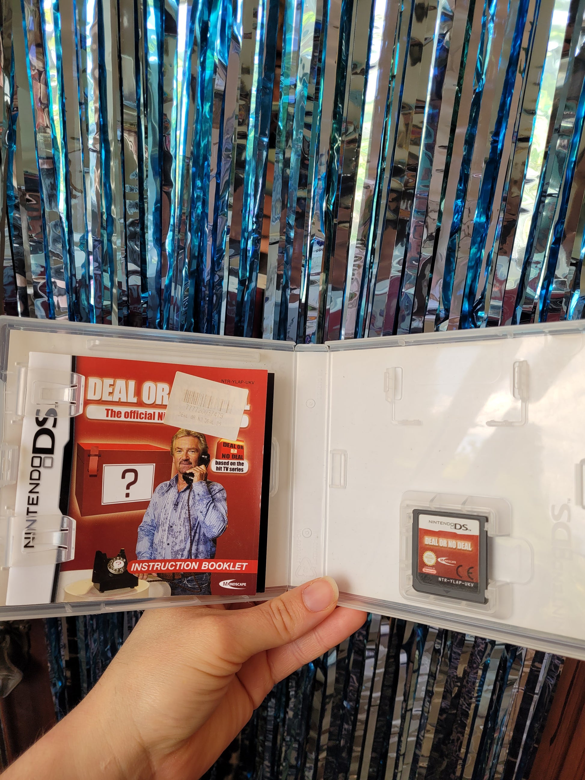 Inside of the Nintendo DS game case with the game itself and the instruction booklet against a blue tinsel sparkly background