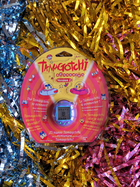 Purple and pink tamagotchi in plastic packaging against multicoloured tinsel background