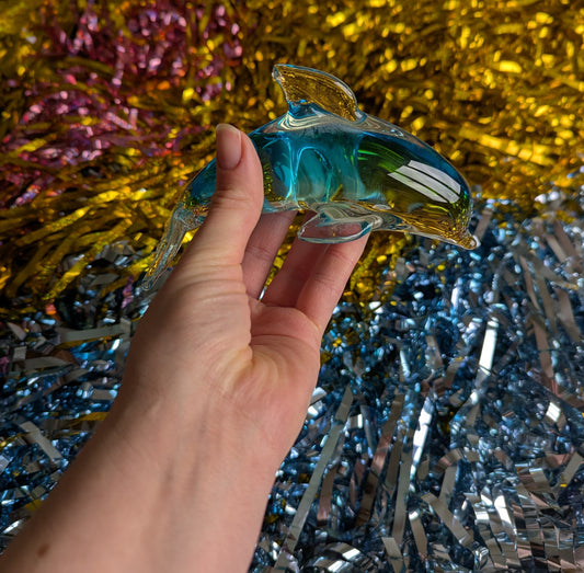 Hand holding a blue and clear glass dolphin ornament against a colourful tinsel background 