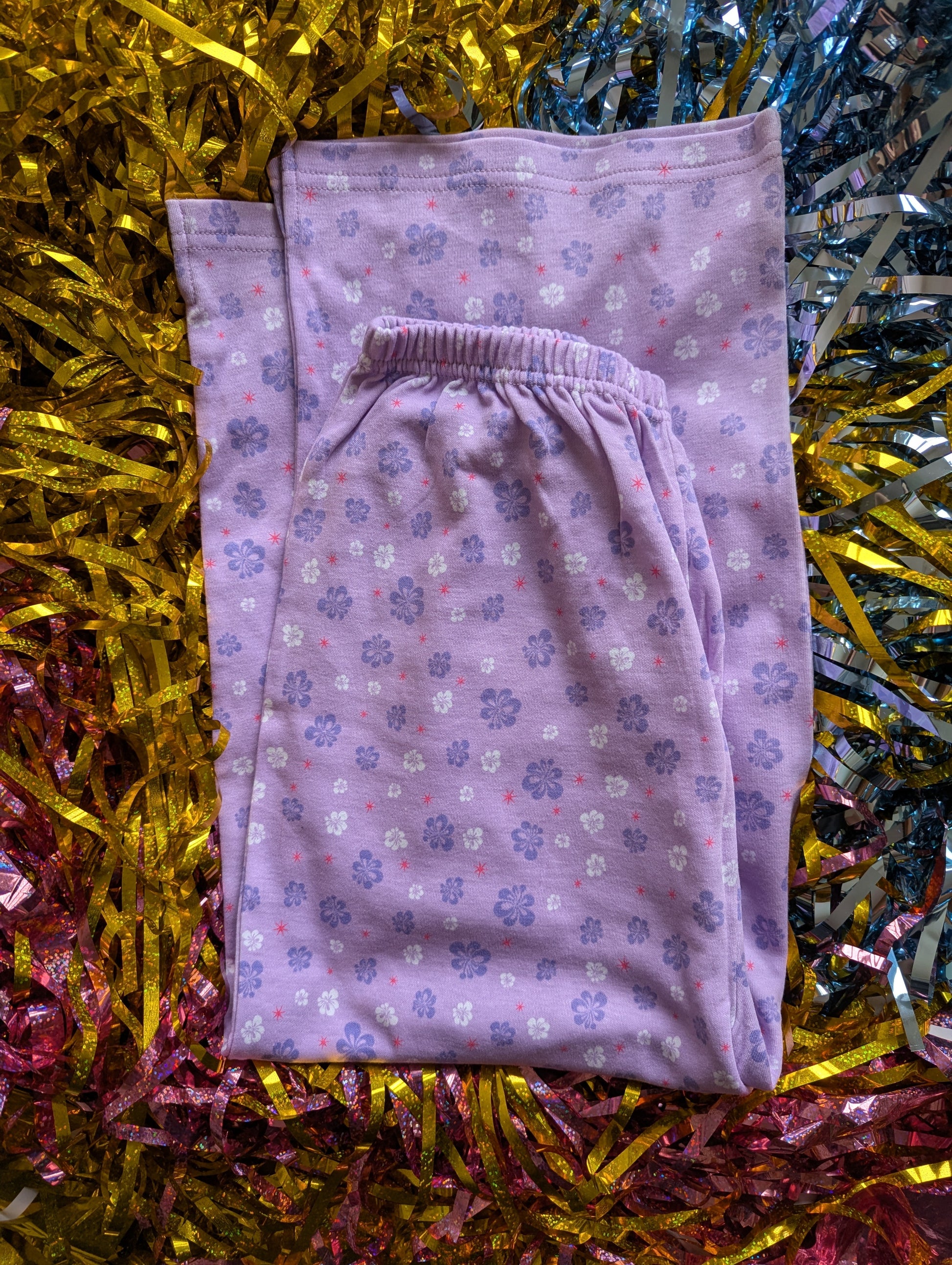 Folded purple pyjama trousers with a pink and purple floral pattern 